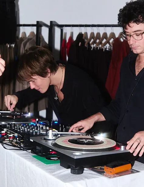 Two DJs performing at a table with turntables and equipment.