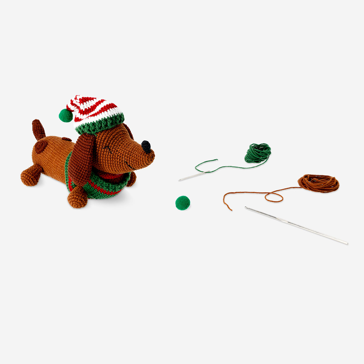 En hæklet gør-det-selv plys-hund iført en julehat med hobbyartikler i nærheden.
