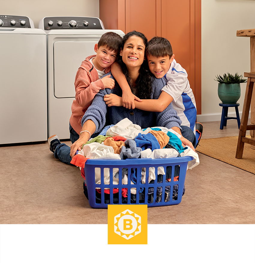 Woman and two children embracing near a laundry basket in a home setting.