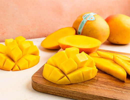 Sliced mango on a wooden board with whole mangoes in the background.