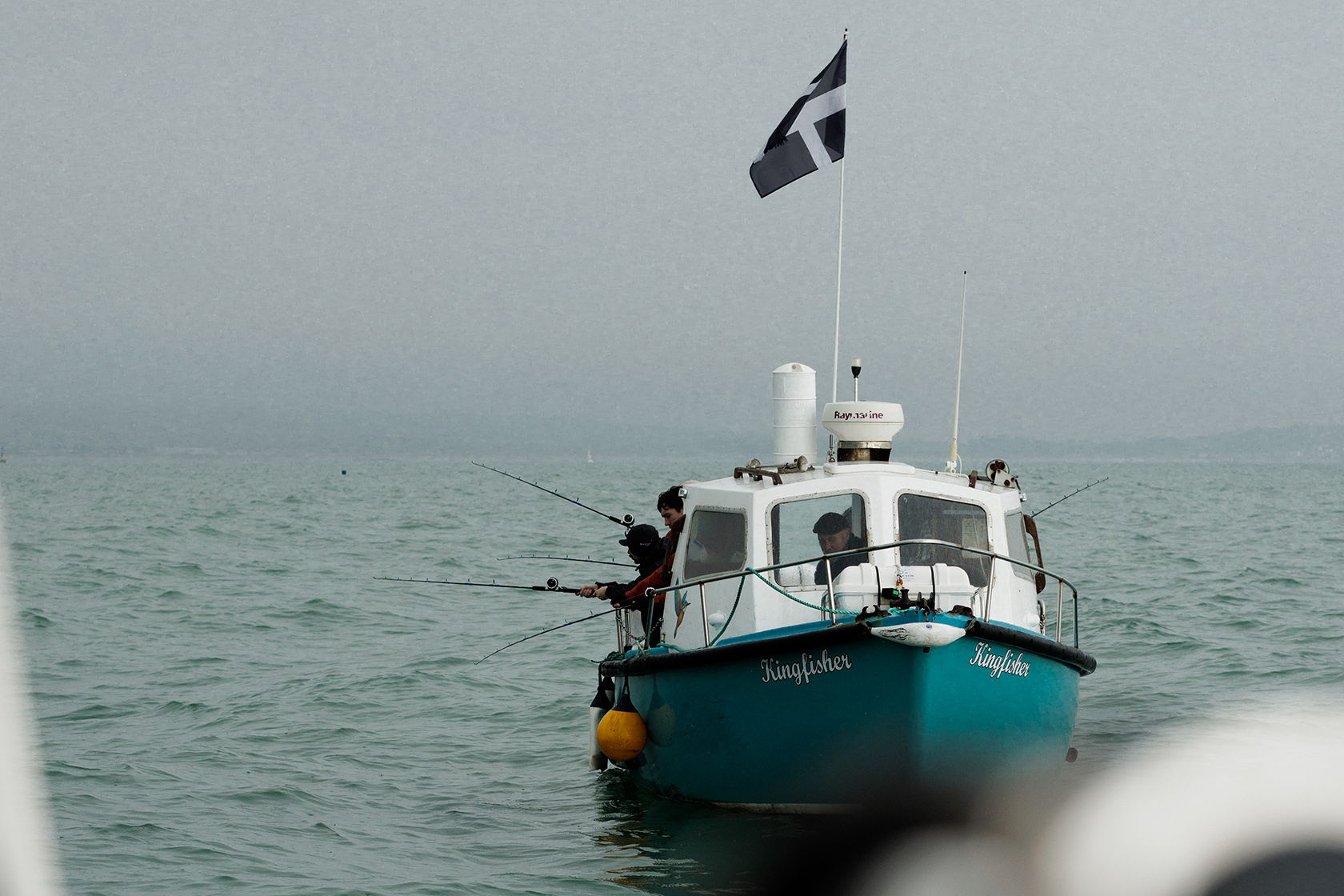 Fishing boat on water with a flag, cloudy sky in background.