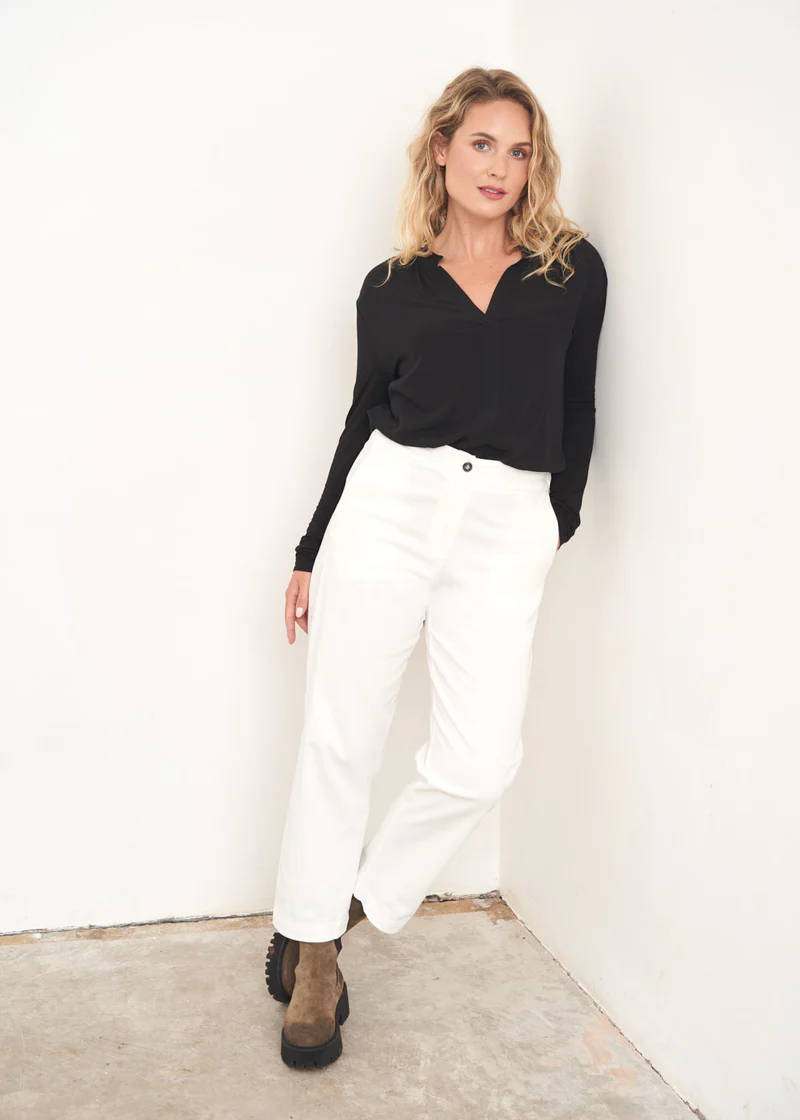 A model wearing a black long sleeved blouse with off white chino style trousers and khaki suede ankle boots