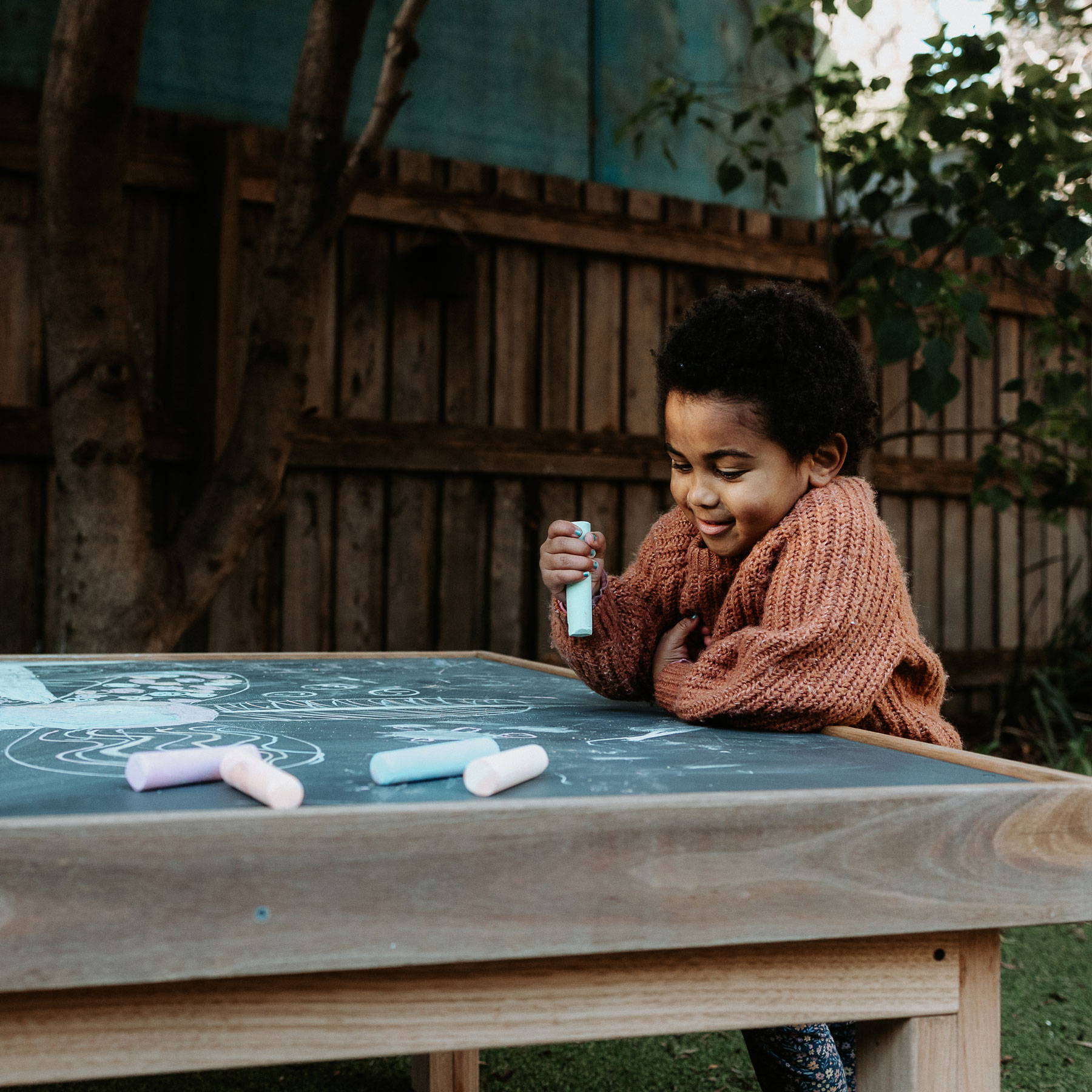 A Child Engaging in Drawing with a Blue Chalk on a Drawing Table