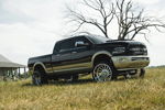 Lifted two-tone black and tan Ram truck with custom Money Talks grille and large chrome wheels parked in a field