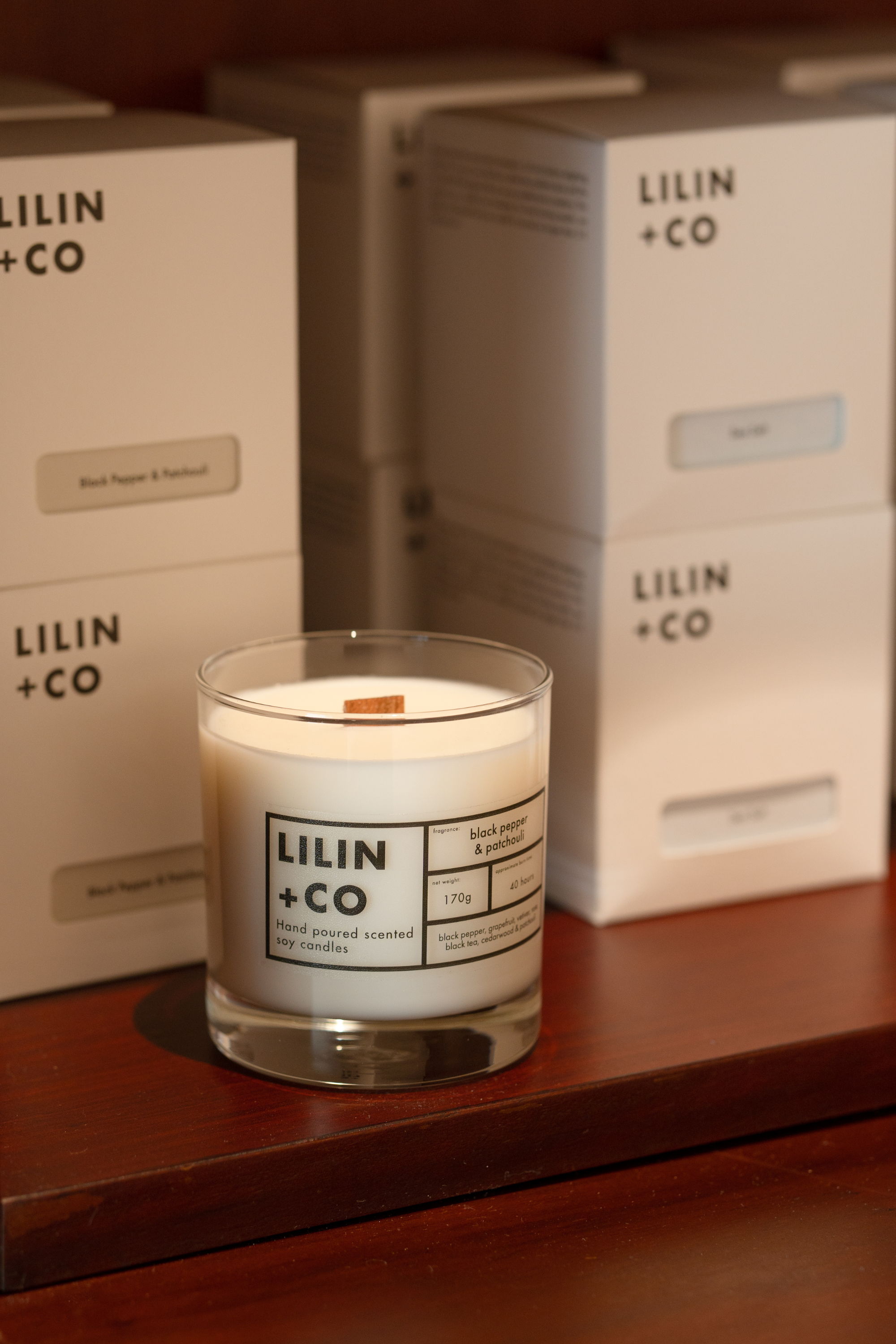 a candle displayed in front of multiple candles in their box packaging on a wooden shelf