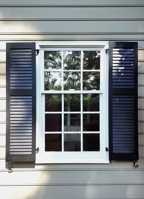A window with black shutters on a wooden wall.