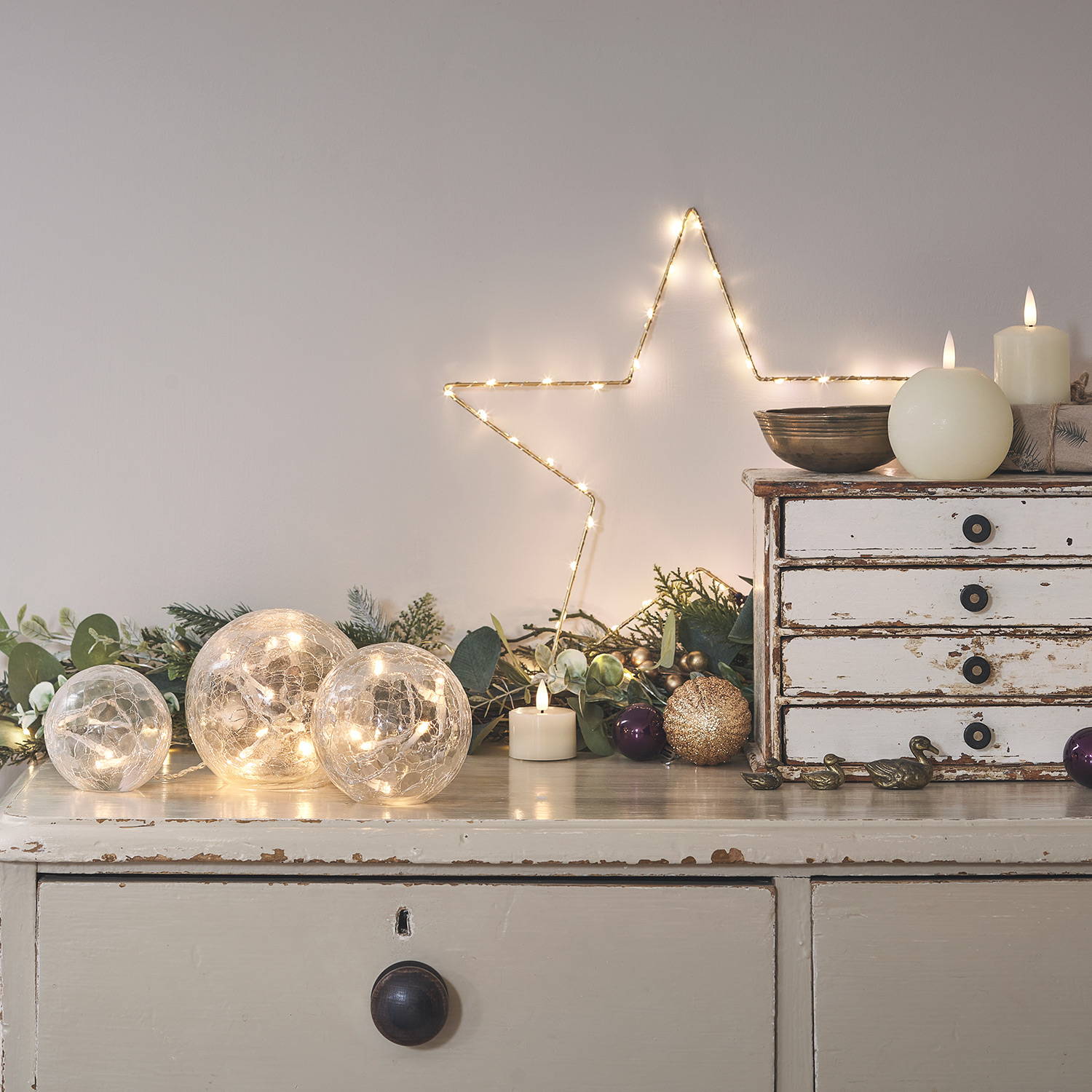 A side table with a Christmas garland, LED candles, a star light and fairy light orbs. 