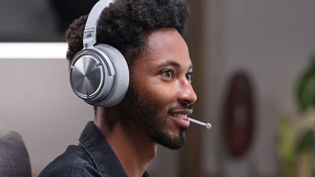 Person wearing gaming headphones and a microphone, smiling while engaging with a computer.