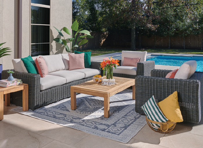Outdoor seating area with a coffee table, flowers, and a pool in background.