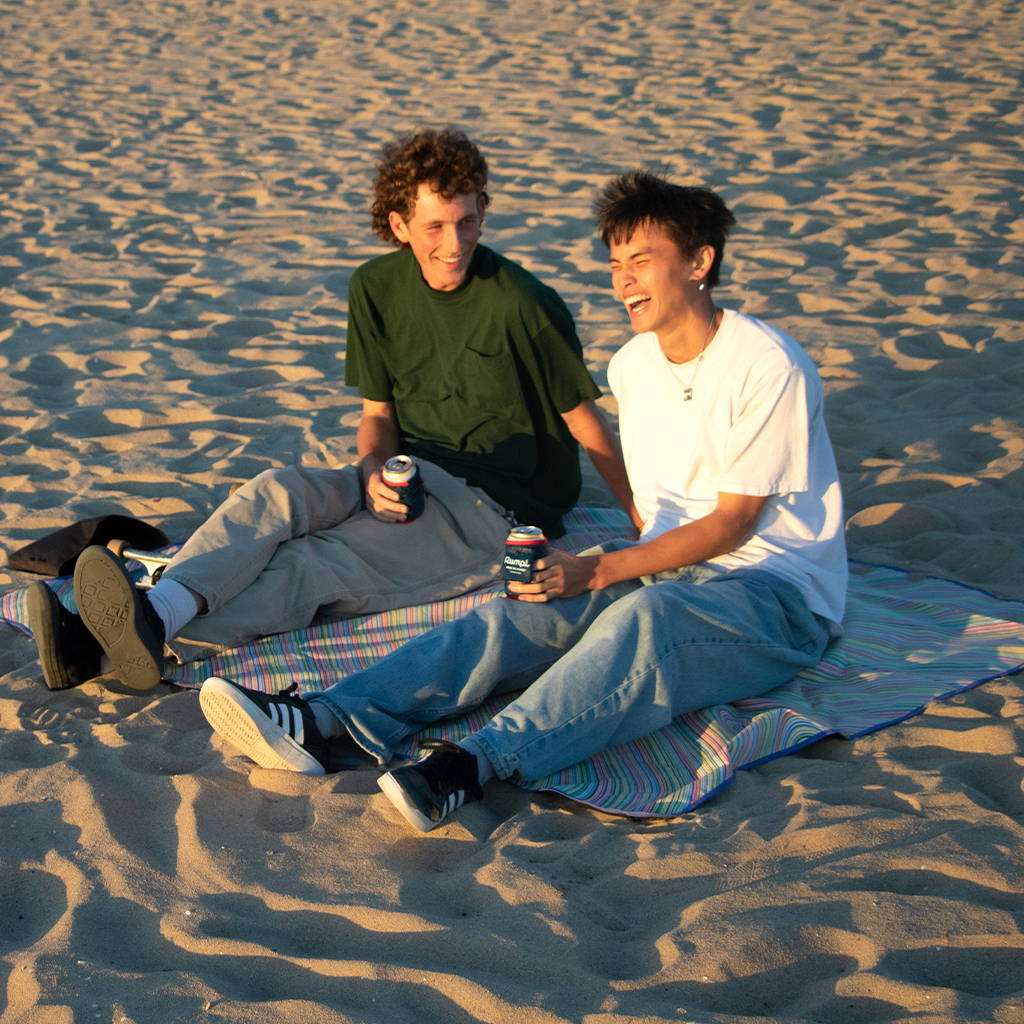 Two people sitting on Rumpl Everywhere Mat with skateboard