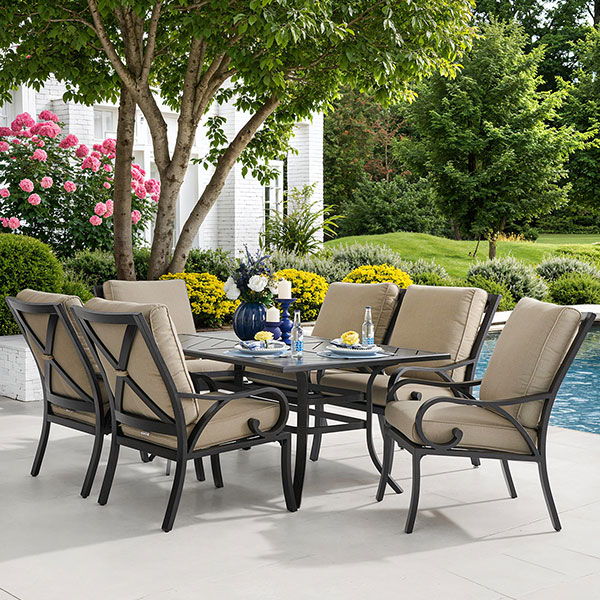 Outdoor dining set by a pool with flowers and greenery.