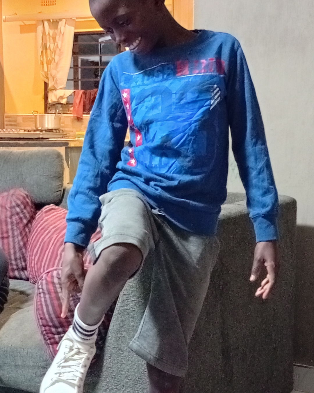 Child in blue shirt and shorts, smiling while adjusting shoes.
