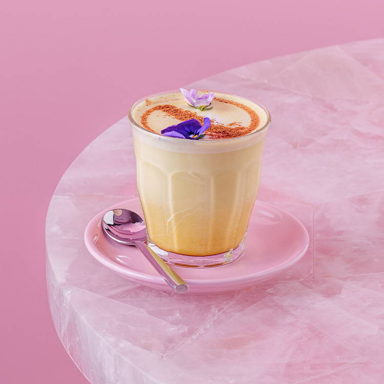 Golden latte with turmeric and cinnamon in a glass on pink table