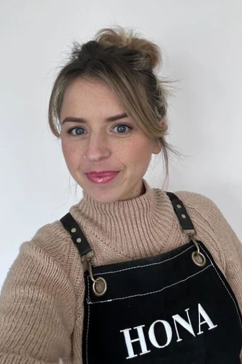A woman wearing a beige sweater and black apron with 