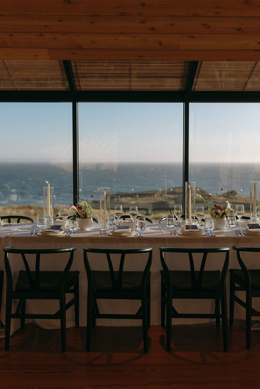 Dining table with chairs overlooking a scenic ocean view through large windows.