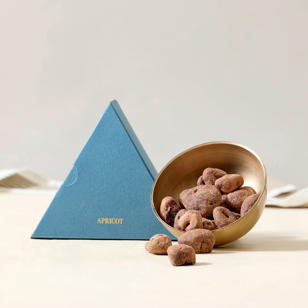 A triangular blue box beside a bowl of chocolate-covered nuts.