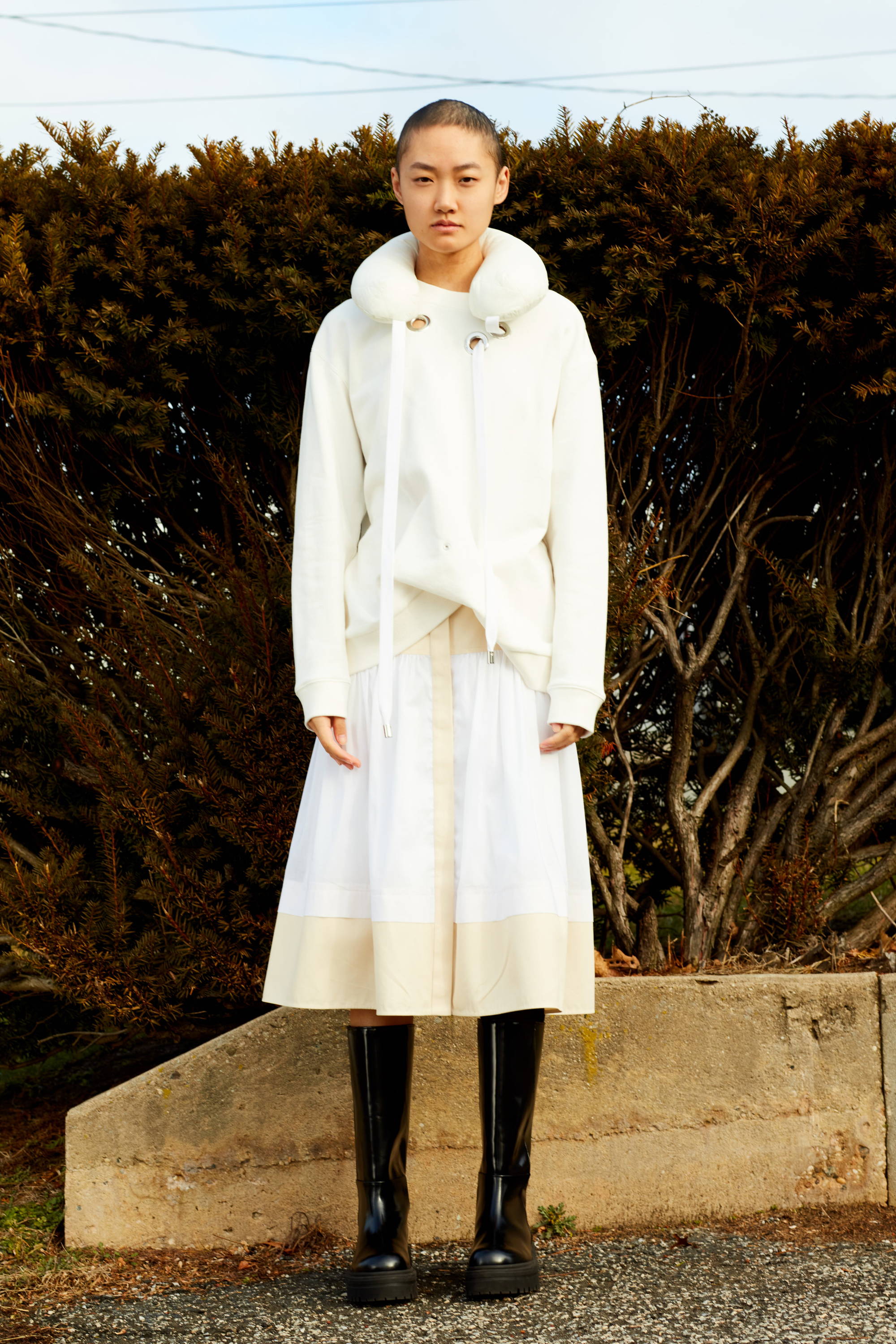 Person wearing a white outfit and black boots, standing outdoors.