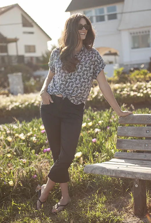 Woman in stylish outfit standing by a bench in a sunny garden.
