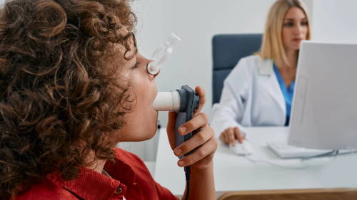 Et barn er hos legen, og gjennomfører en lungefunksjonstest som benyttes i diagnostisering av astma. Barnet har på neseklype og blåser luft inn i et rør.