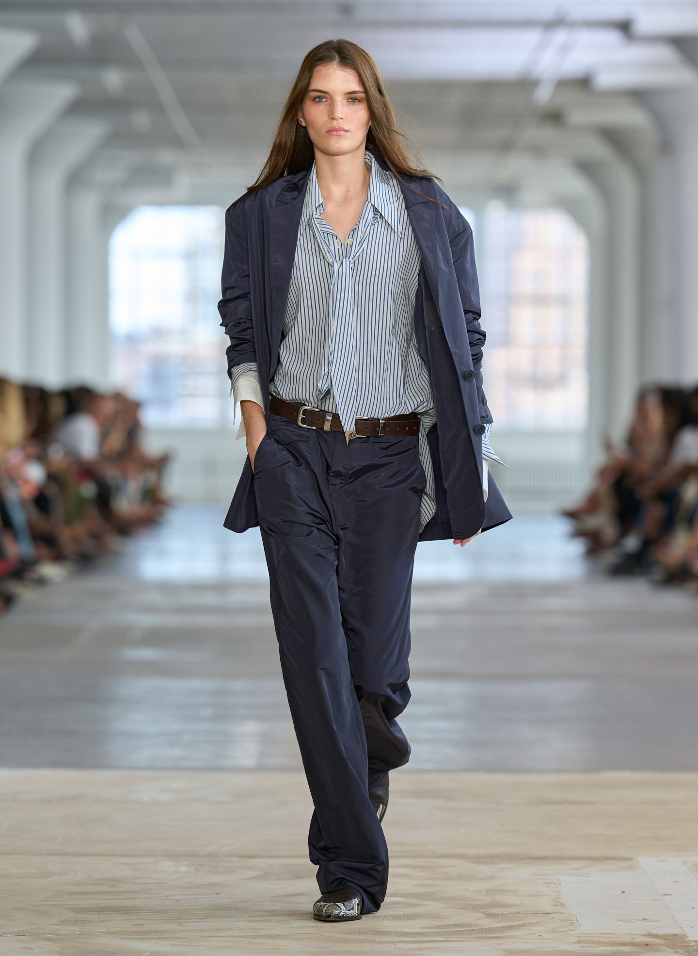 Model walking down the runway in a stylish outfit during a fashion show.