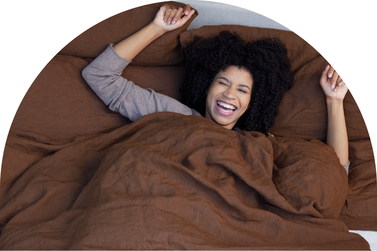 Glücklich lachende Frau zugedeckt im Bett