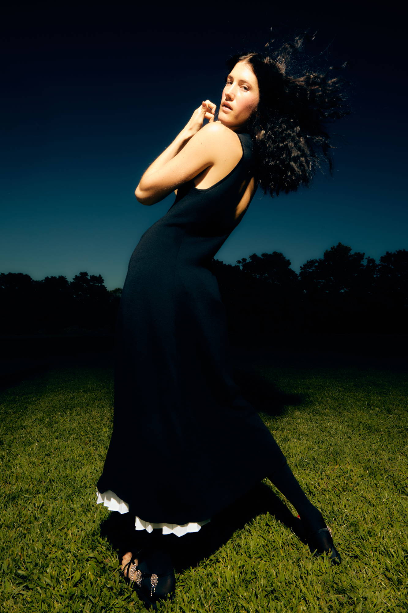 A woman in a black dress poses against a dark sky.
