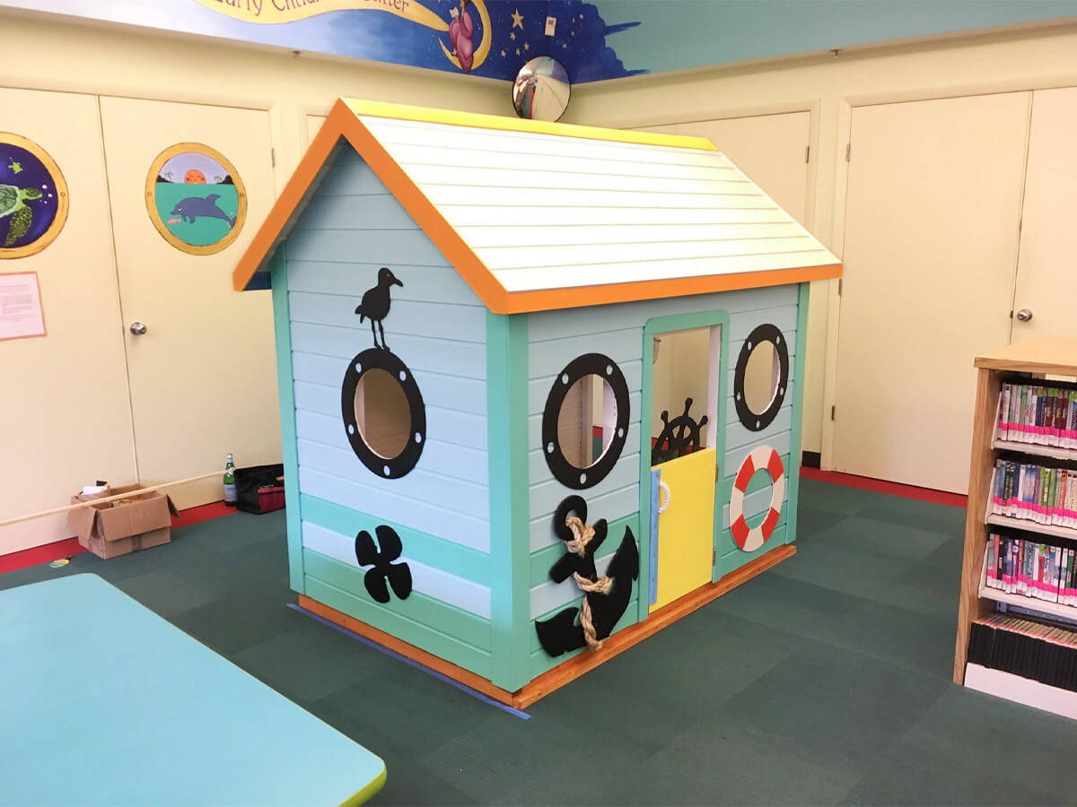 Custom Wooden Playhouse with white roof and the round windows in the library by WholeWoodPlayhouses