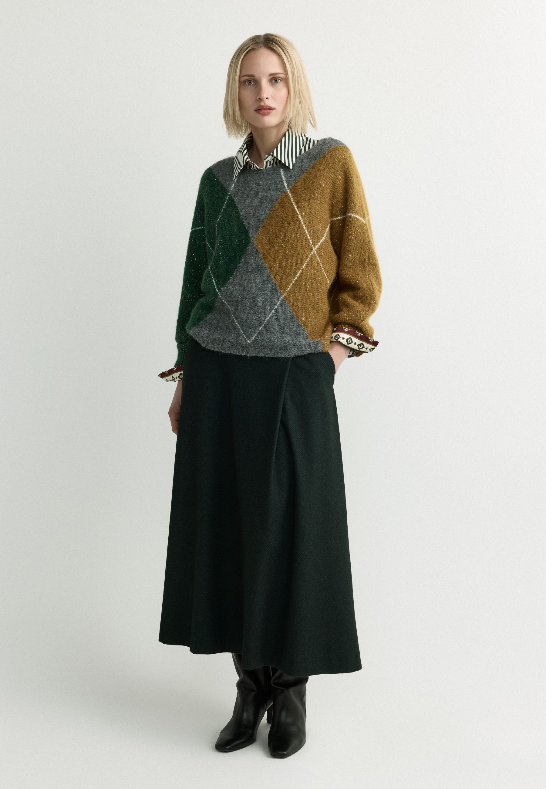 A woman in a patterned sweater and long skirt stands against a plain background.