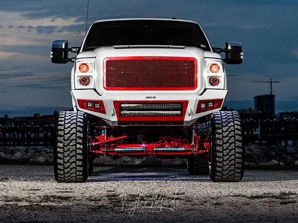 Front view of Corbin's lifted white 2016 Ford F250 with red grille and LED lighting at twilight