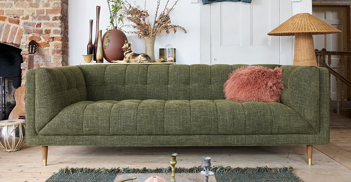 Green 3 seater large sofa with a decorative pillow, surrounded by indoor plants and decor.