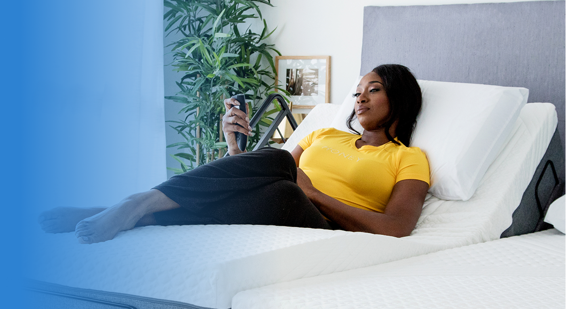 Woman reclining on an adjustable bed using a handheld remote to change her position for comfort and support.