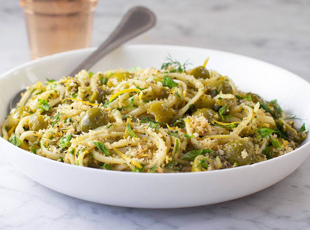 Linguine pasta in a bowl tossed with green olives and breadcrumbs