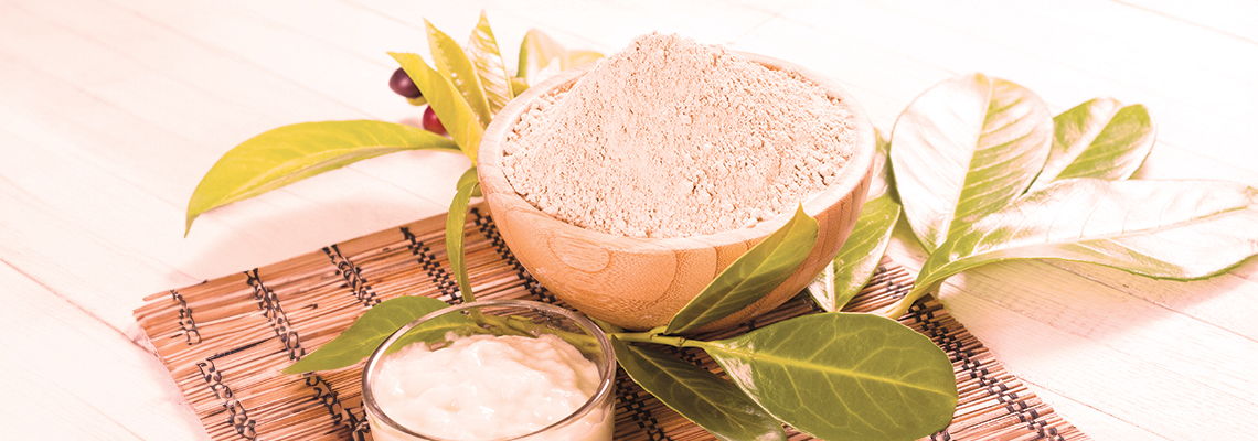Bowl of flour surrounded by green leaves on a woven mat.