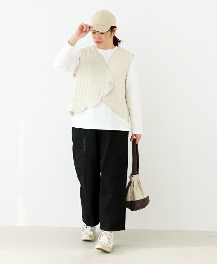 Person walking in casual outfit with a cap and bag against a plain background.