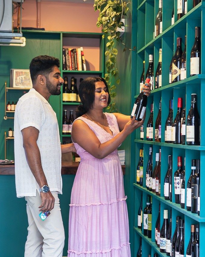 Two people selecting wine from a shelf in a store.