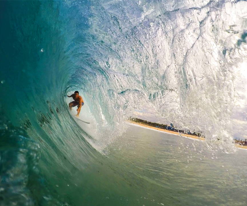 A photo of a male surfer inside of a wave, with the beach in the background.