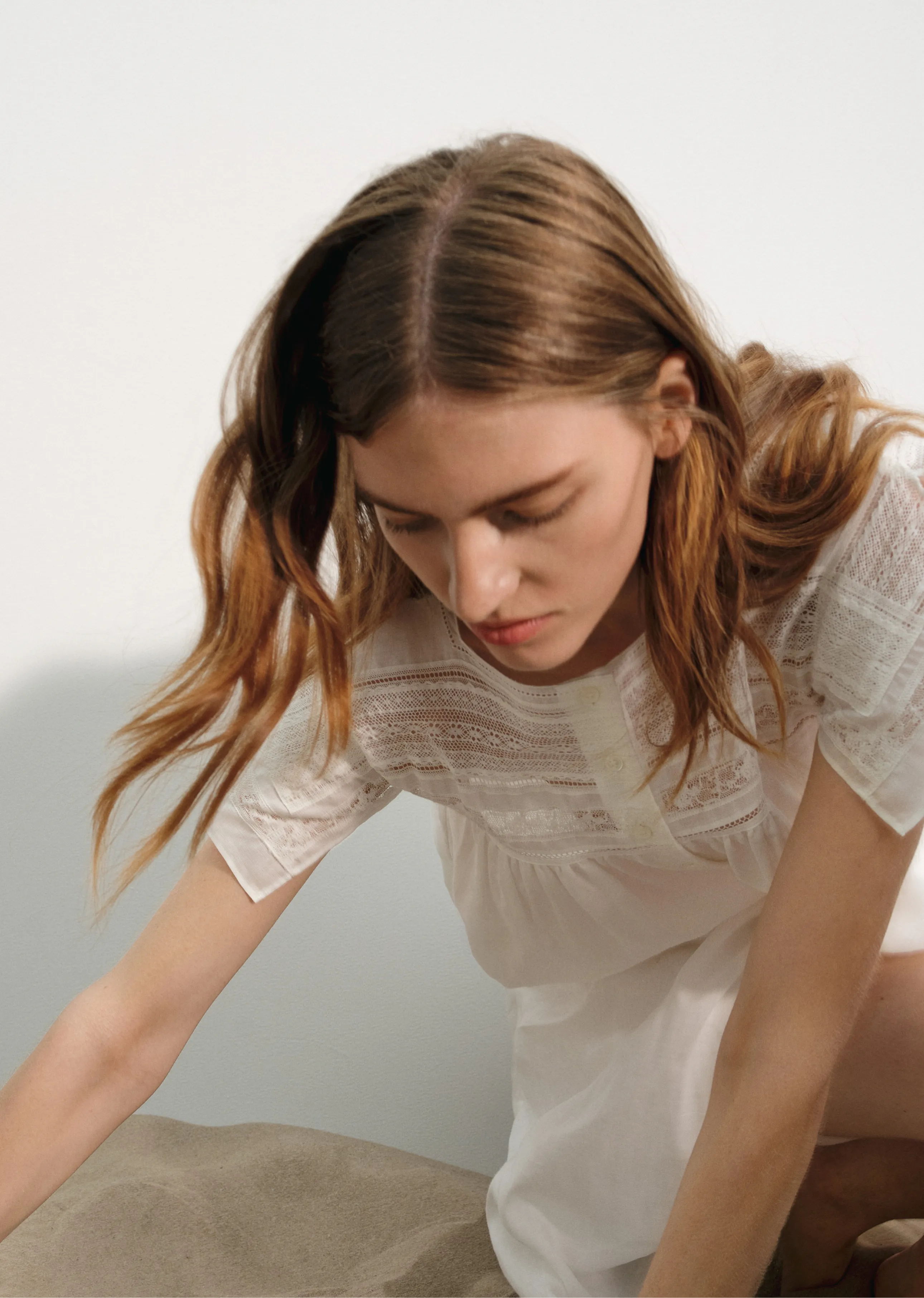 A woman with long hair wearing a white dress, looking down.