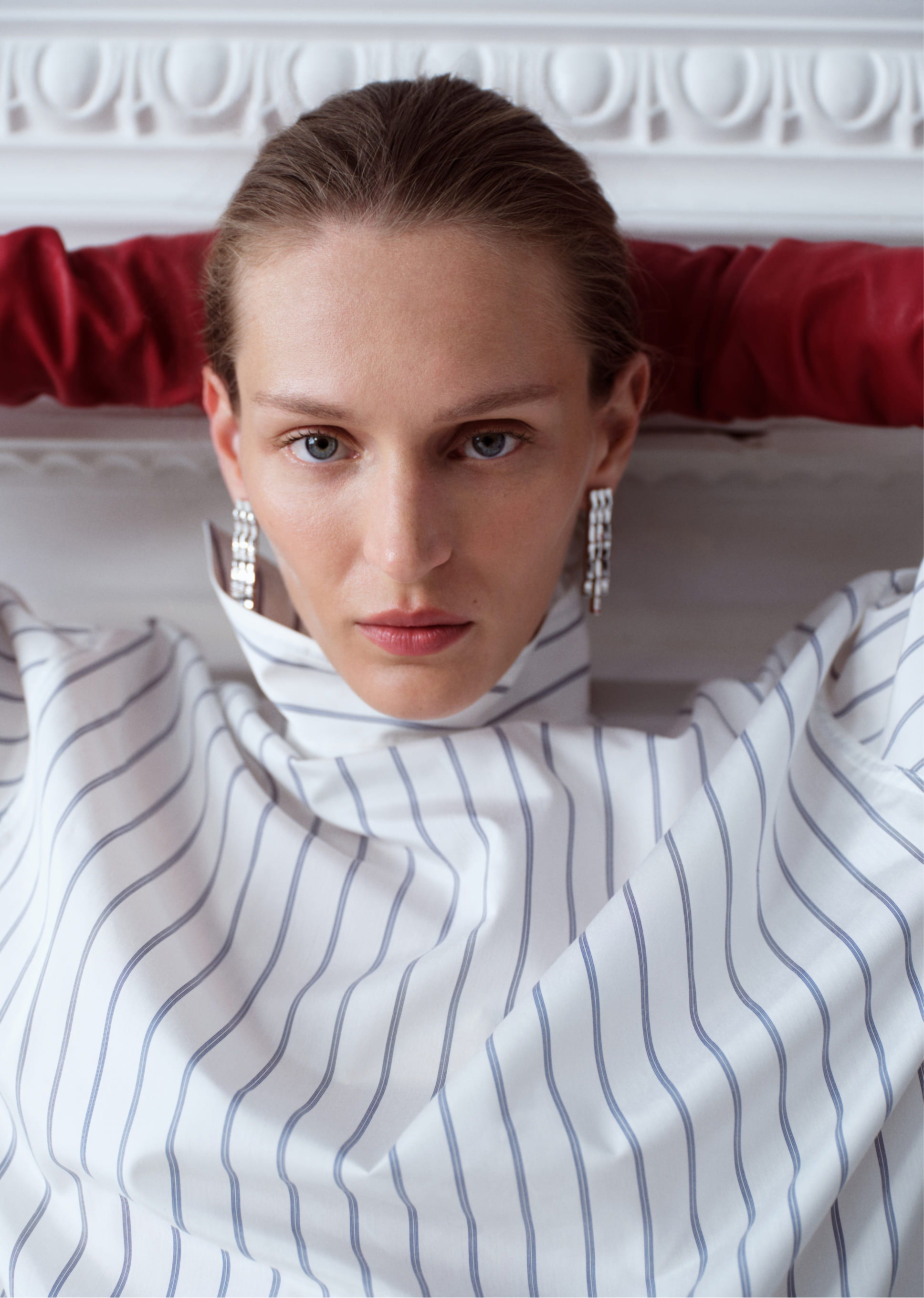 A woman with earrings poses in a striped shirt against a decorative background.