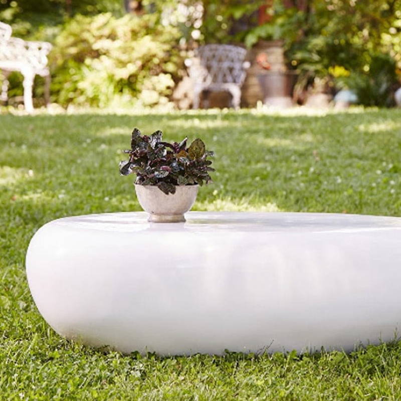 A white pebble outdoor coffee table in the grass with a potted plant on top.