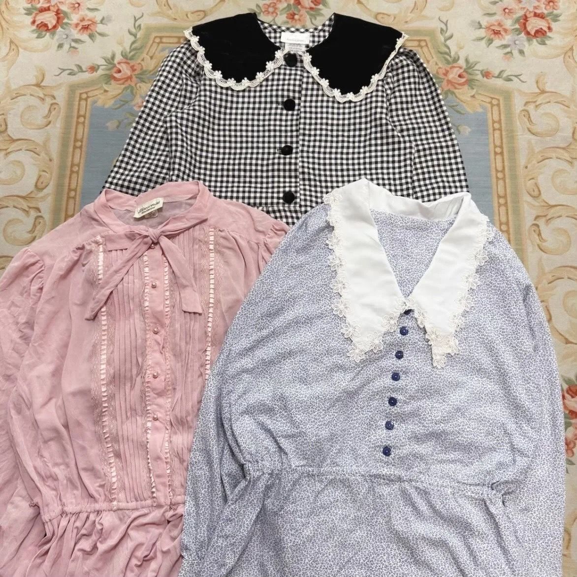 Three vintage-style blouses in pink, blue, and black patterns on a floral background.