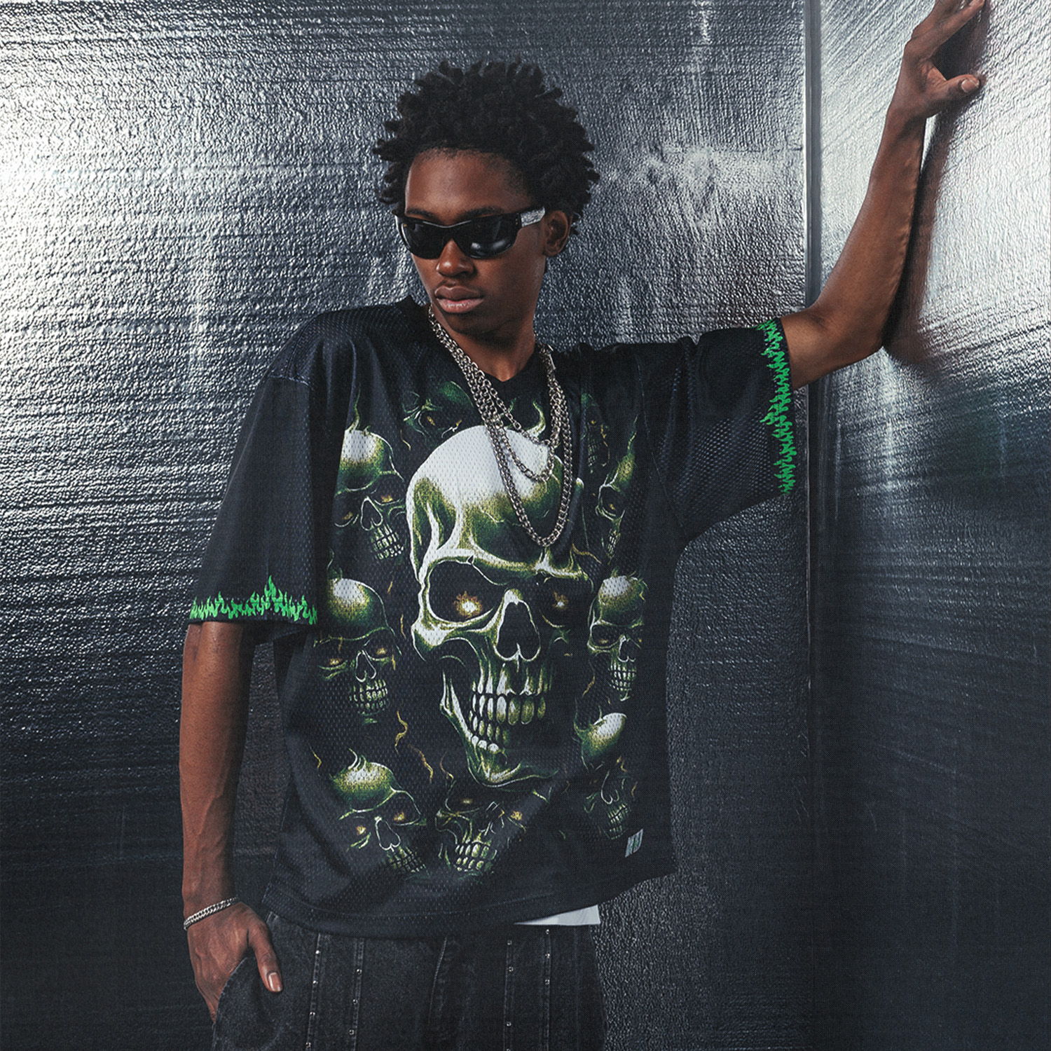 Person wearing a black skull-graphic shirt and sunglasses, leaning against a wall.
