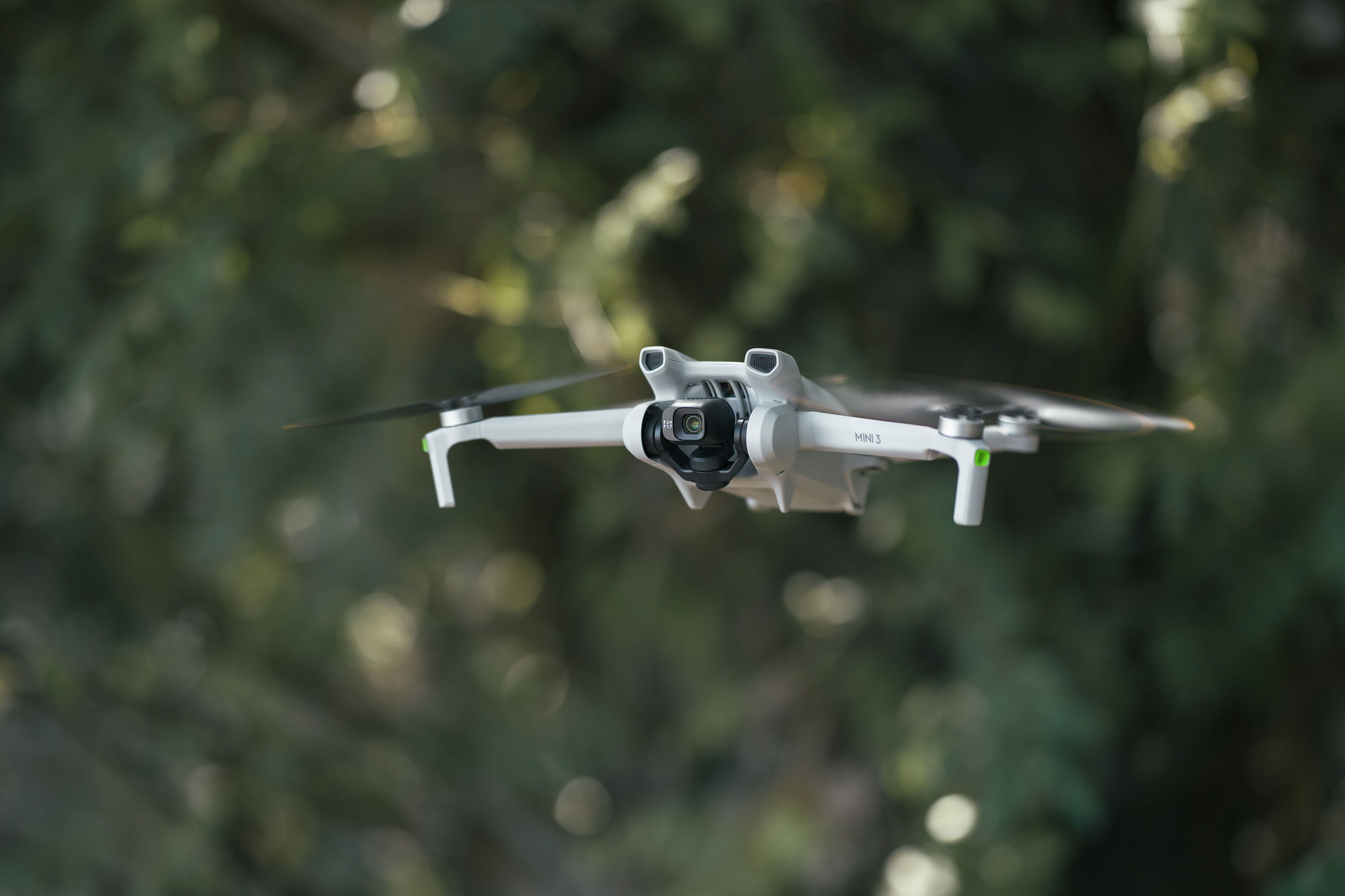 A DJI Mini 3 drone flying with trees in the background.
