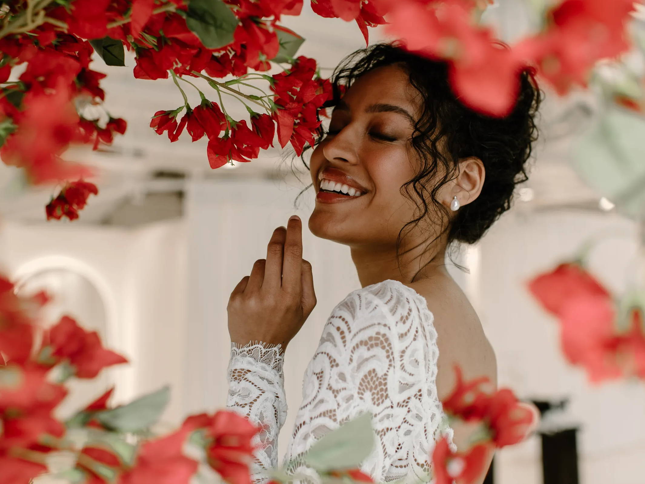 Mariée portant une robe en dentelle à manches longues sous un bougainvillier rouge 