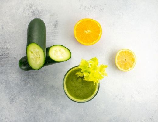 Green smoothie with cucumbers, orange, and lemon on a light background.