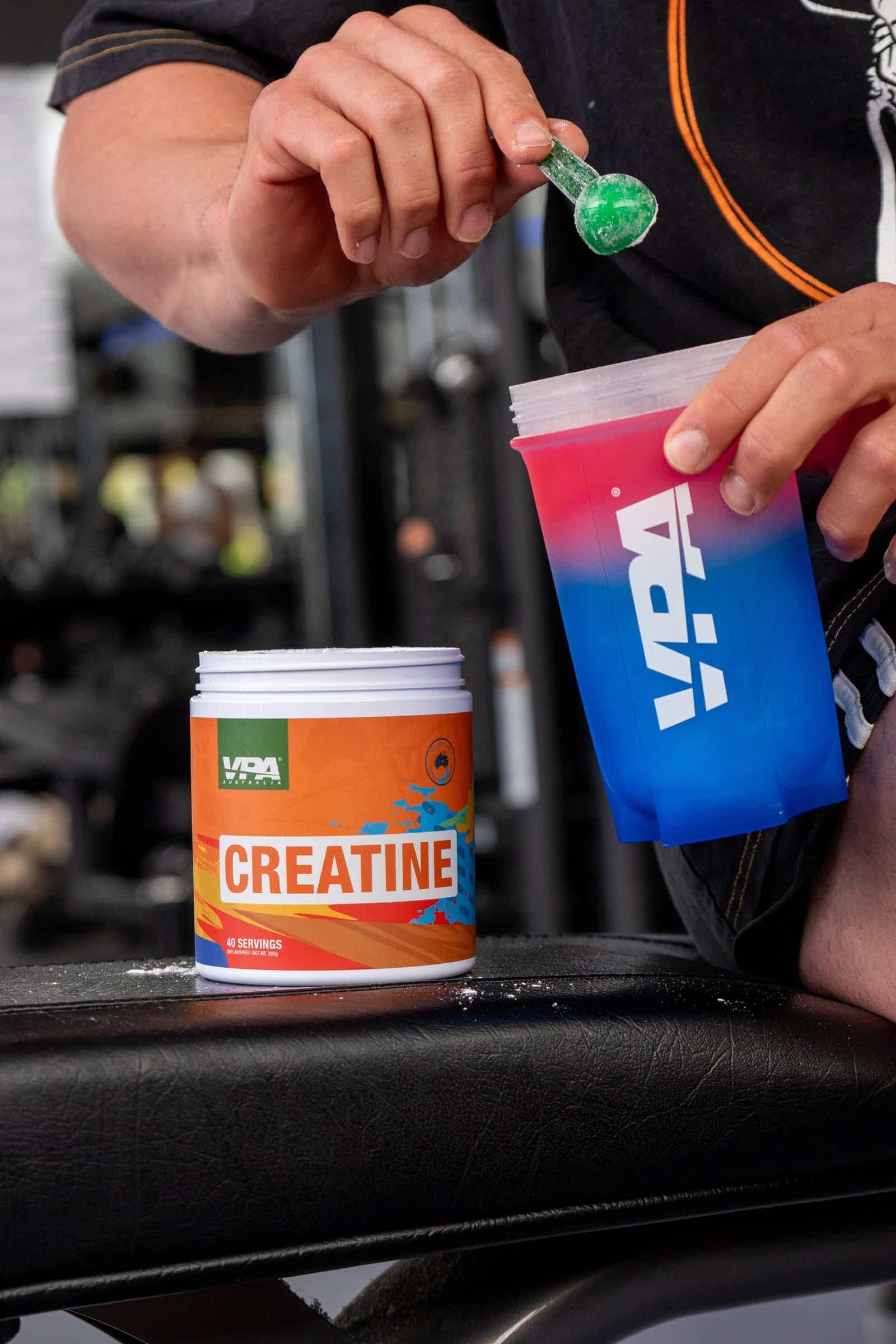 Person mixing creatine powder into a colorful shaker bottle at the gym.