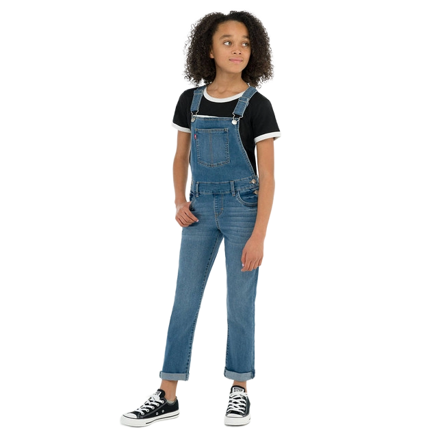 Girl wearing overalls and a black t-shirt, standing confidently.