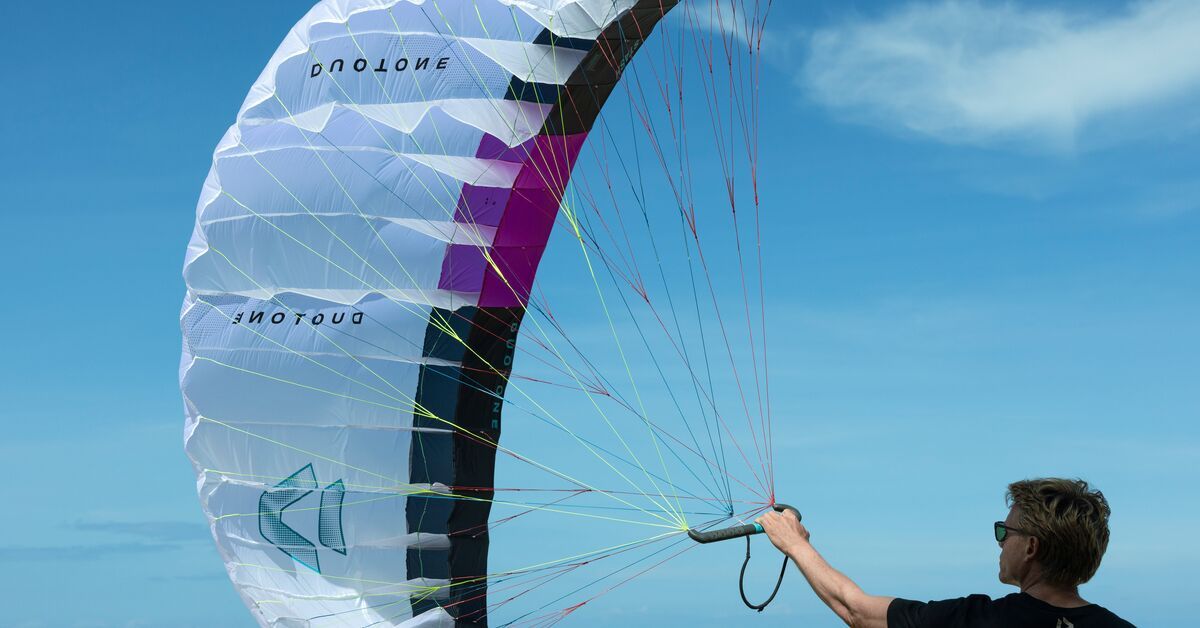 Person holding a colorful kite against a clear blue sky.