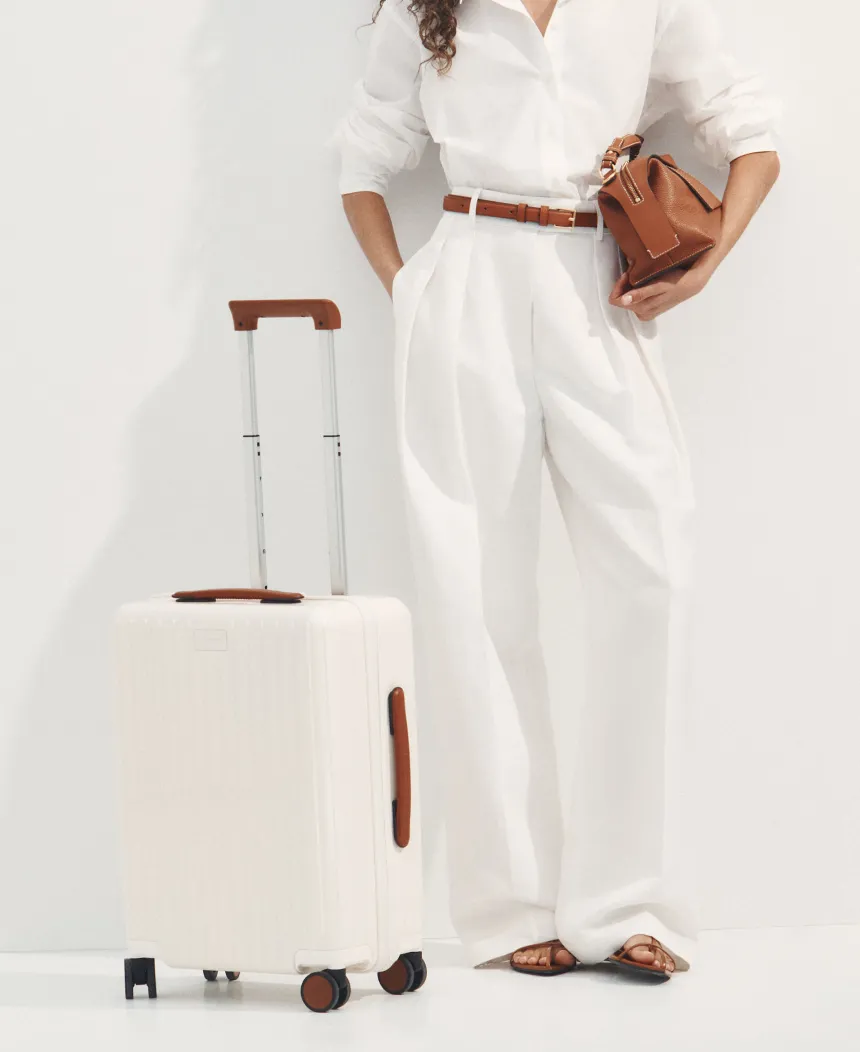Woman in white outfit with suitcase and handbag.