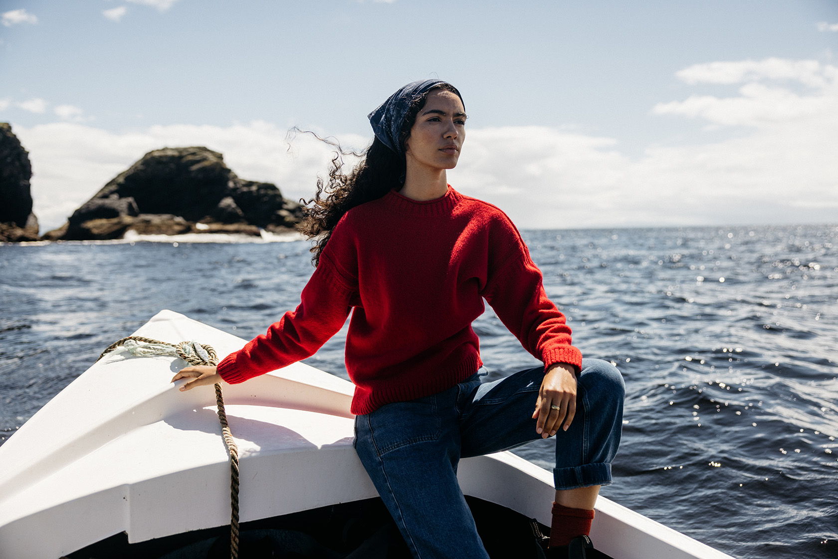 Person in a red sweater sitting on a boat, looking out at the water.