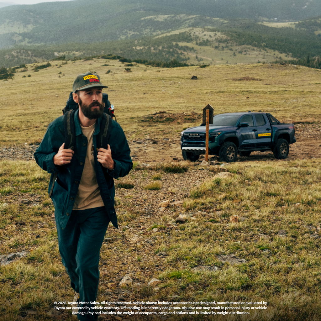 Man with a backpack walking in a grassy field near a truck.